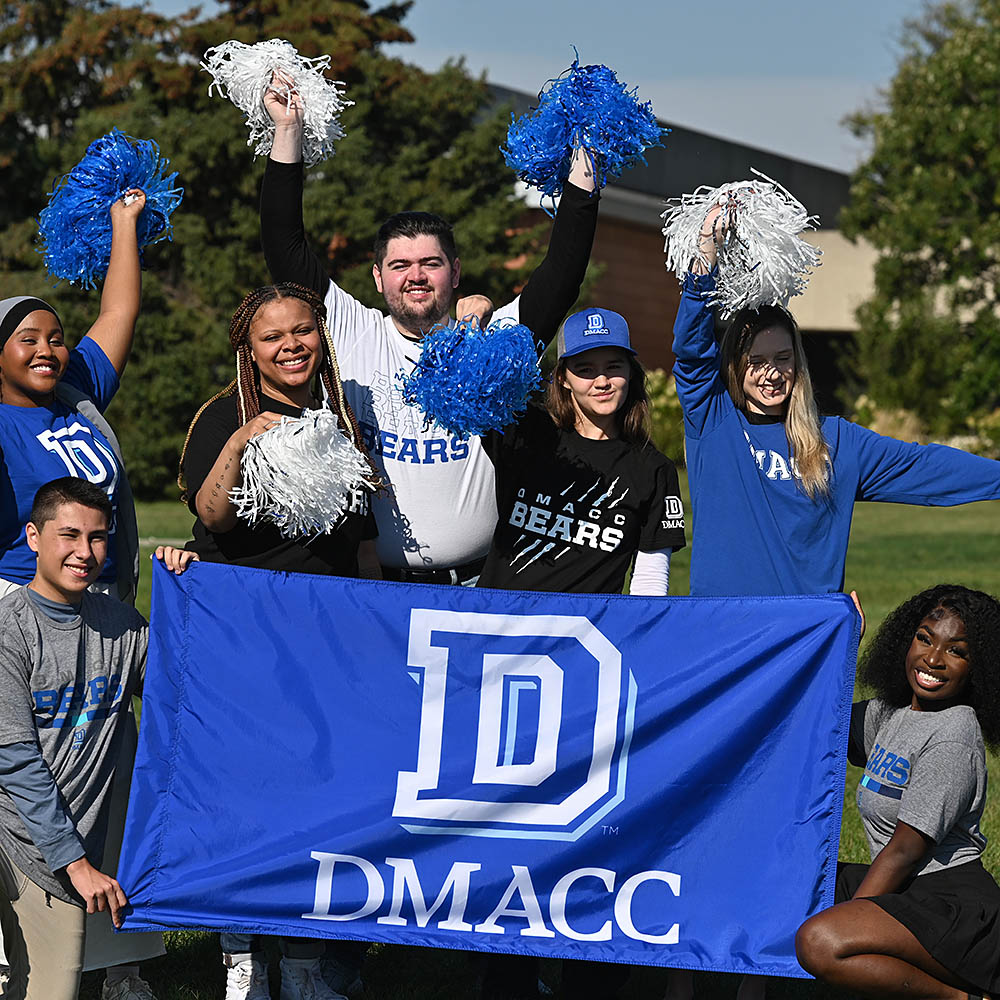 A group of DMACC students hold a banner and cheer.