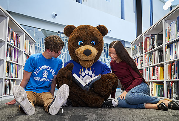 two students in the library with the DMACC bear reading a book