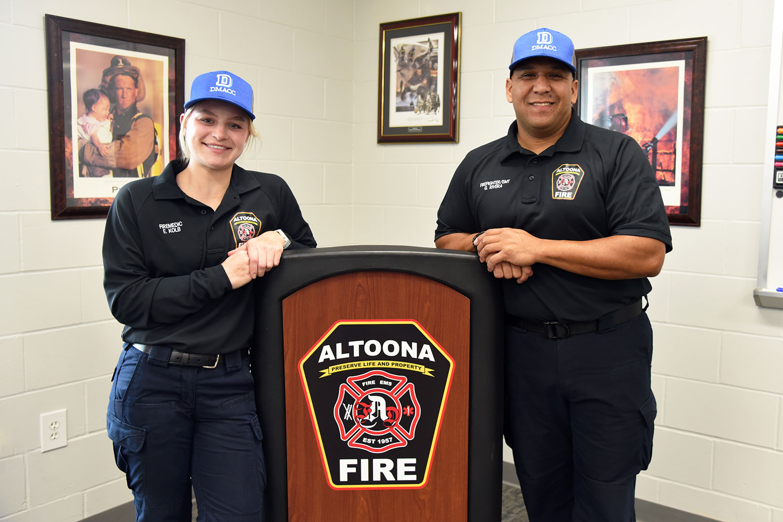 Kolb (above, left), an August 2023 graduate of the DMACC Paramedic certificate program, and her​ Altoona Fire Department colleague Gabriel Rivera (right), a 2016 DMACC Emergency Medical Technician (EMT) program alum, are all smiles while sporting new DMACC hats on Nov. 1 at the Altoona Fire Department.