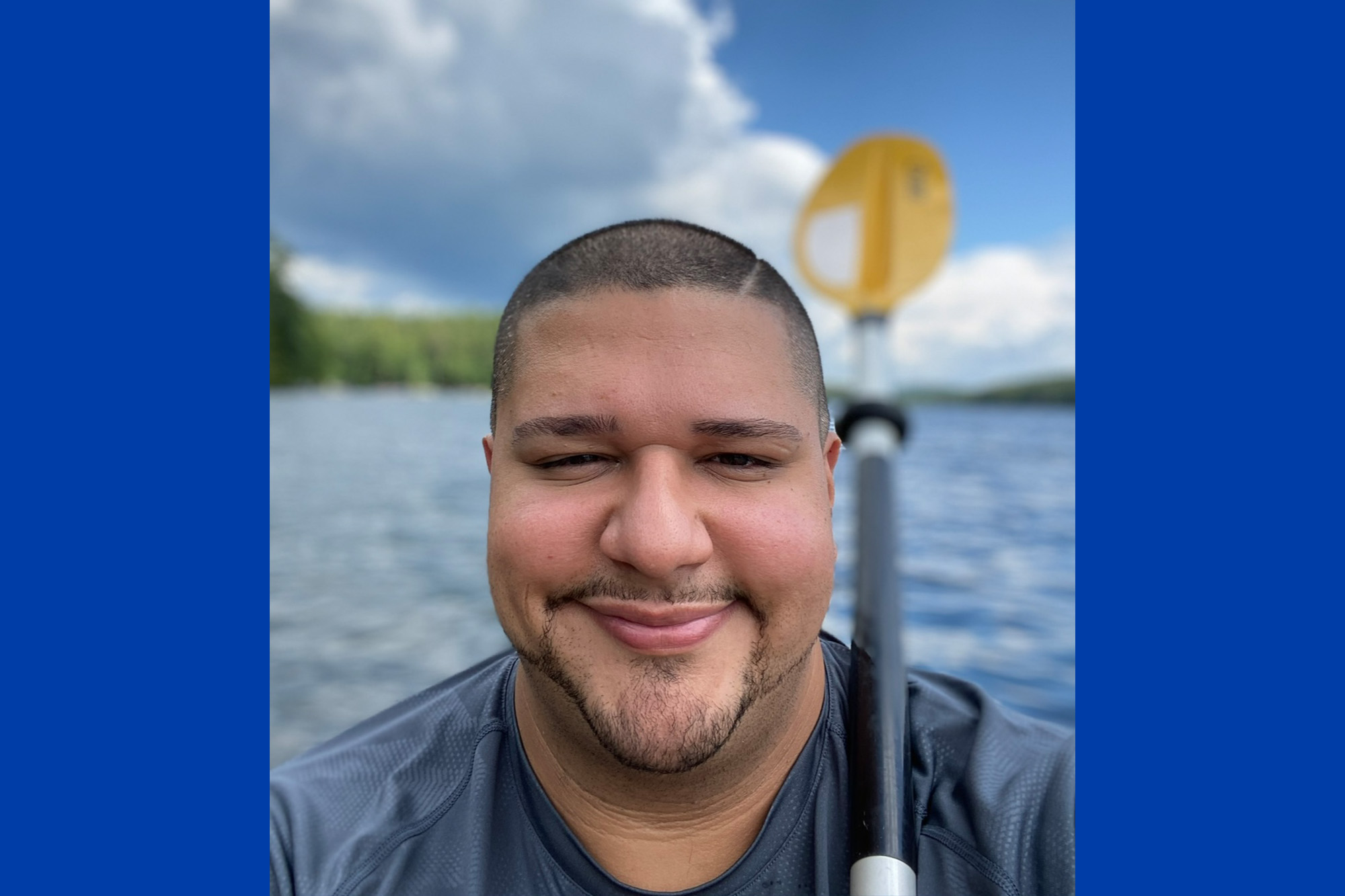 Selfie of a man with a yellow paddle body of water and trees behind him.