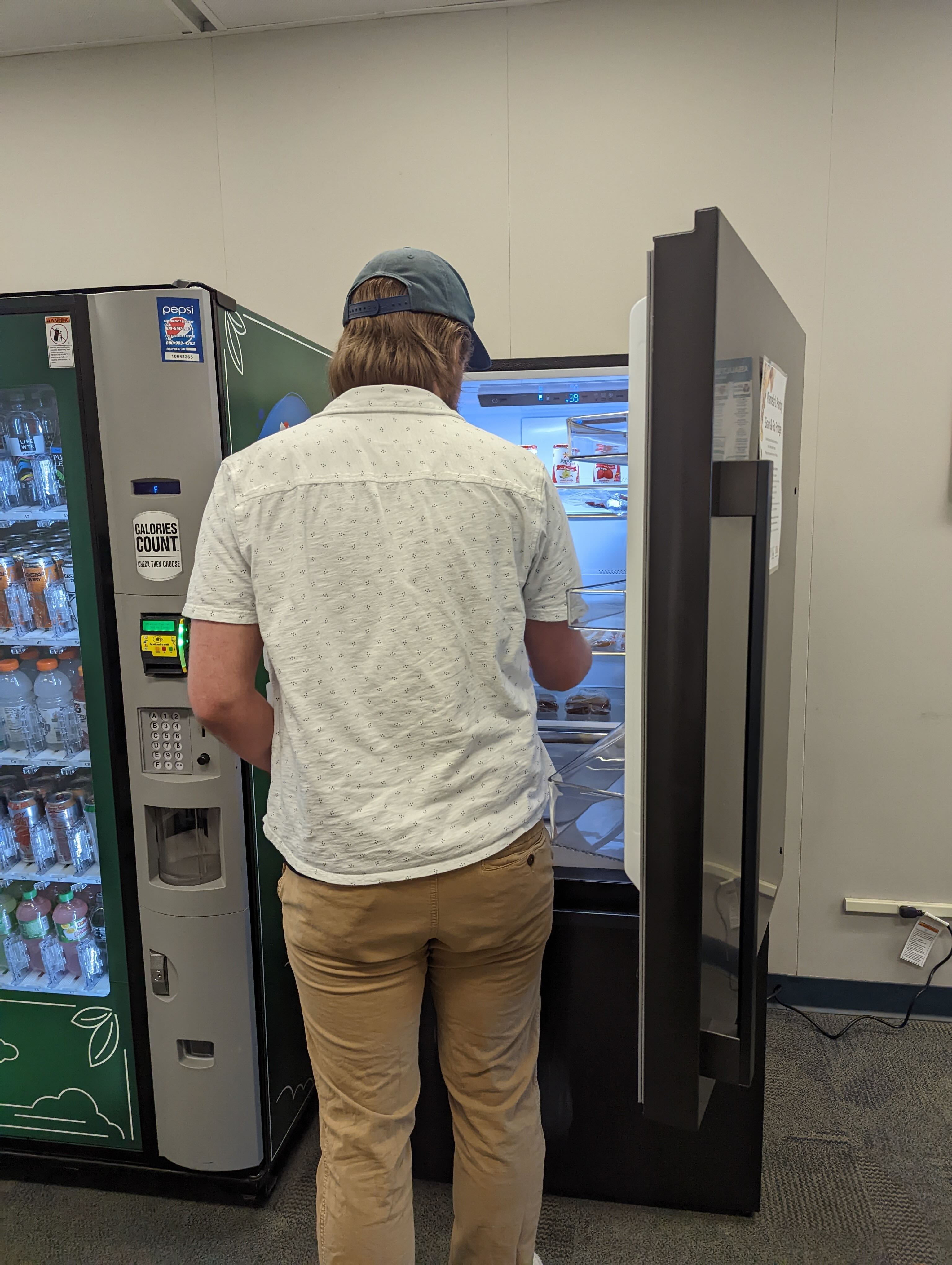 Student using fridge at DMACC Urban Campus A person in a white collared shirt and khaki pants stands in front of an open fridge with their backed turned.